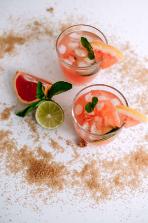 Grapefruit cocktail, lemonade with lime, mint and pieces of ice on a white table with cane sugar. High quality photoの写真素材