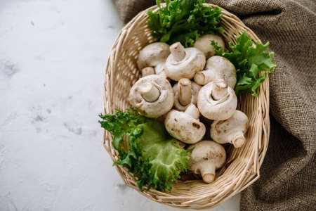Champignon mushrooms in a basket with herbs on the table. Top view. High quality photoの写真素材