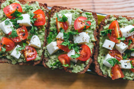 Bruschetta toast with guacamole and tomatoes, sea salt and herbs on dark bread and a wooden board, healthy nutrition. Close up. High quality photoの写真素材