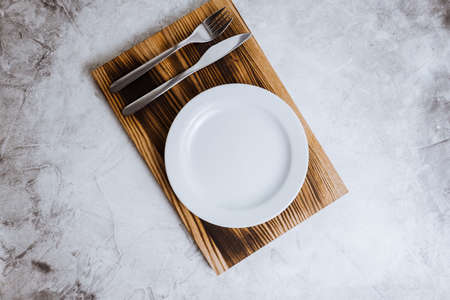 Empty white plate on a wooden board with cutlery on a gray background. High quality photoの写真素材