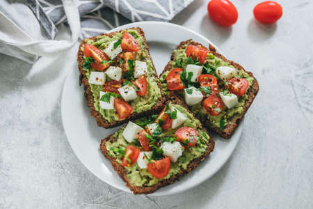 Bruschetta toast with guacamole and tomatoes, sea salt and herbs on dark bread and a white plate, healthy nutrition. High quality photoの写真素材