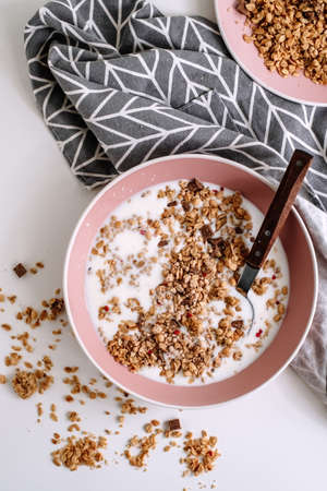 Granola muesli with fresh milk and pieces of chocolate in a pink plate on a white table. Healthly food, breakfast concept. High quality photoの写真素材