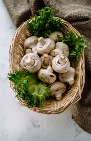 Champignon mushrooms in a basket with herbs on the table. Top view. High quality photoの写真素材