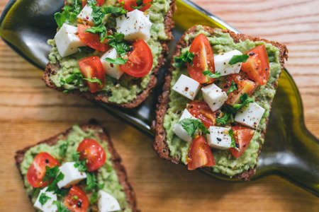 Bruschetta toast with guacamole and tomatoes, sea salt and herbs on dark bread and a wooden board, healthy nutrition. Close up. High quality photoの写真素材