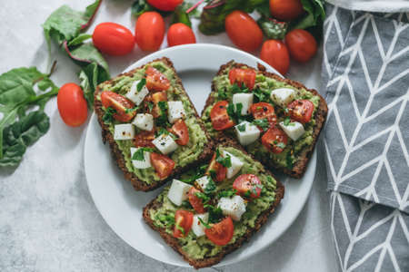 Bruschetta toast with guacamole and tomatoes, sea salt and herbs on dark bread and a white plate, healthy nutrition. High quality photoの写真素材