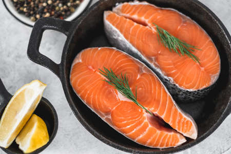 Fresh steaks of red salmon fish with spices, herbs and lemon in a black pan. High quality photoの写真素材