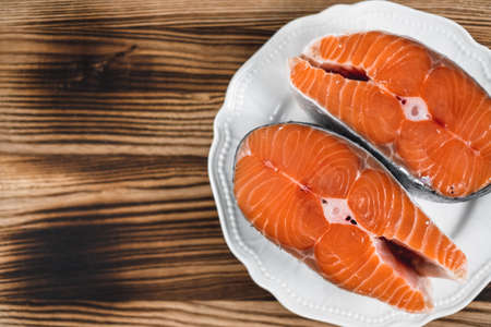 Fresh steaks of red salmon fish in a white plate on a wooden board with copy space. High quality photoの写真素材