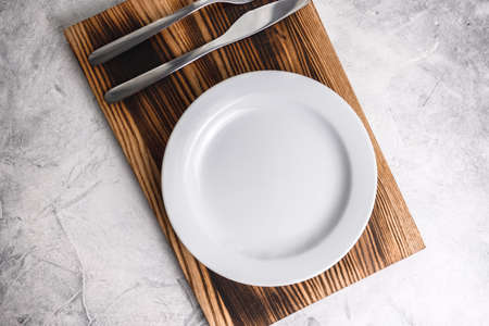 Empty white plate on a wooden board with cutlery on a gray background. High quality photoの写真素材