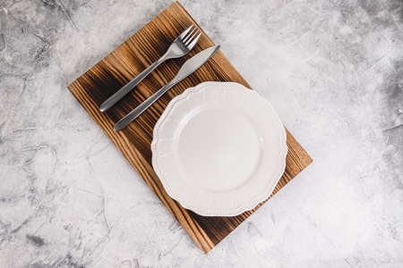 Empty white plate on a wooden board with cutlery on a gray background. High quality photoの写真素材
