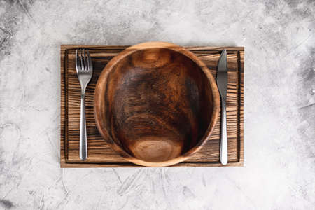 Empty wooden bowl plate on a wooden board with cutlery on a gray background. High quality photoの写真素材