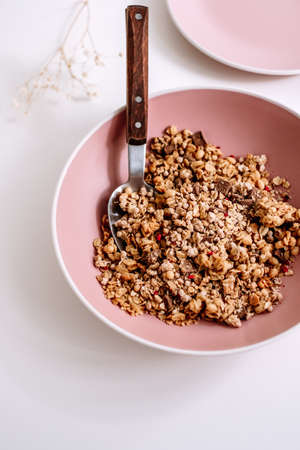 Granola muesli with pieces of chocolate in a pink plate on a white table. Healthly food, breakfast concept. High quality photoの写真素材