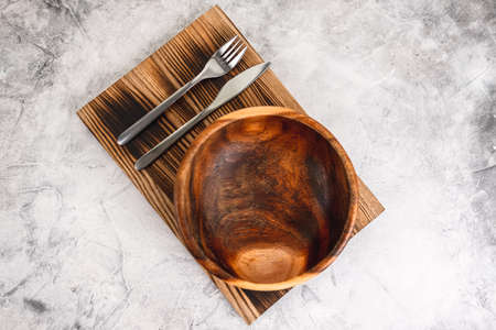 Empty wooden bowl plate on a wooden board with cutlery on a gray background. High quality photoの写真素材