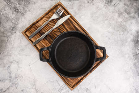 Empty black pan plate on a wooden board with cutlery on a gray background. High quality photoの写真素材