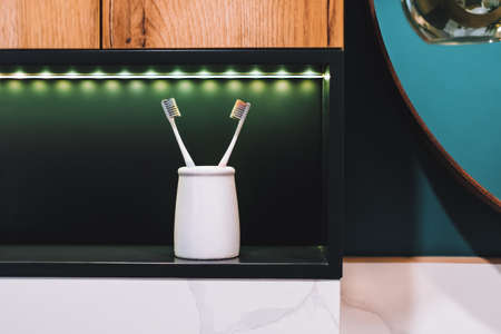 Pair of toothbrushes in a white glass on the shelf in the bathroom. Nobody. High quality photoの写真素材