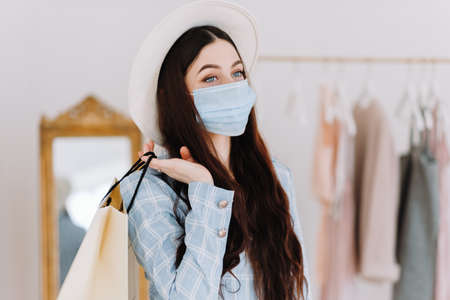 Stylish caucasian young woman in protective mask and business suit with shopping bag in fashion boutique while shopping. High quality photoの写真素材