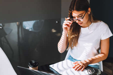 Focused caucasian young woman college student in glasses studying with books laptop distantly preparing for test exam writing essay doing homework at home, distantly education concept.の写真素材