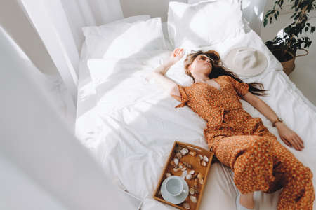 Beautiful young stylish woman in glasses lying on bed in sunny morning. High quality photoの写真素材