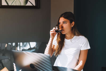 Caucasian young woman drinking coffee while working with laptop, distantly working concept. High quality photoの写真素材