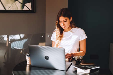 Focused caucasian young woman college student studying with books laptop distantly preparing for test exam writing essay doing homework at home, distantly education concept. High quality photoの写真素材