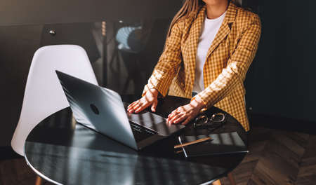 Young businesswoman sitting in armchair with hands on the laptop and ready to work. Working in...