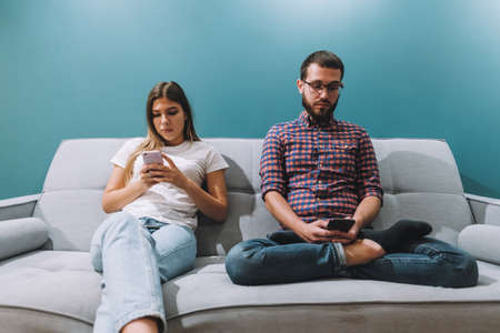 Young couple using smartphones while sitting on the couch at home. Passively scrolling through social media. High quality photoの写真素材