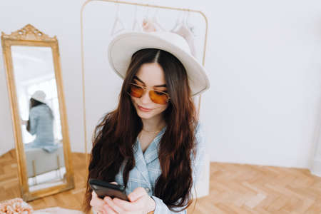 Stylish caucasian young woman in business suit using smartphone in fashion boutique while shopping....