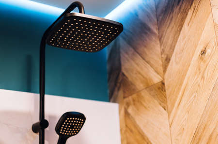 Black rain shower head and hand shower, with LED lighting on the ceiling in bathroom, close up. High...