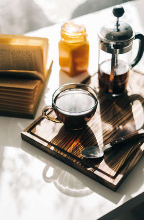 Coffee brewed in a French press and a cup on a wooden board with open book on a table. Morning at home, coziness and comfort. High quality photoの写真素材