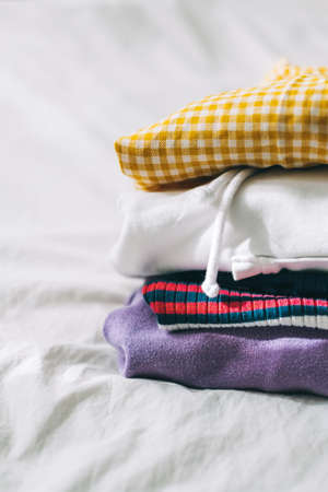 Stack of multicolored clothes on a white bed from wardrobe. High quality photo