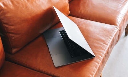 Laptop computer on brown sofa. Freelancer home workspace office. High quality photoの写真素材