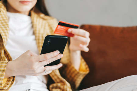 Young caucasian woman holding credit card, using smartphone and shopping online. E-commerce, internet banking, spending money. High quality photoの写真素材