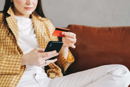 Young caucasian woman holding credit card, using smartphone and shopping online. E-commerce, internet banking, spending money. High quality photoの写真素材
