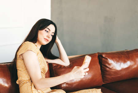 Young caucasian woman using smartphone while resting on a stylish sofa at home. High quality photo