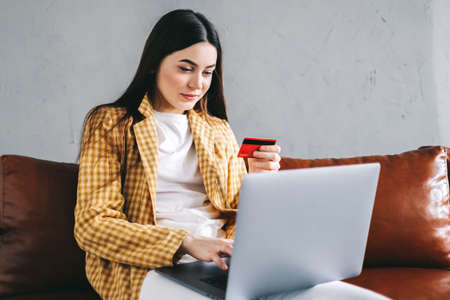 Young caucasian woman holding credit card, using laptop computer and shopping online. E-commerce, internet banking, spending money. High quality photoの写真素材