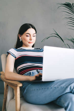 Portrait of beautiful brunette young woman in earphones, freelancer working distantly at home, looking at laptop screen on video call or chat and typing on keyboard. High quality photoの写真素材