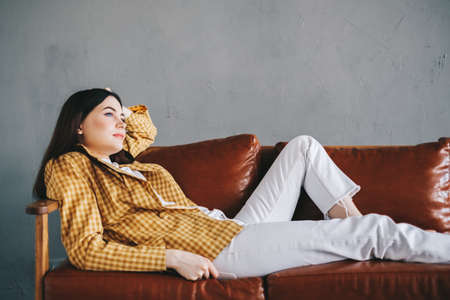 Young calm caucasian stylish woman relaxing lying on comfortable sofa in modern living room, lazy happy woman resting on couch at home. High quality photoの写真素材
