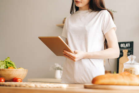 Caucasian woman use tablet computer in the modern kitchen, preparing salad, read recipe.の写真素材