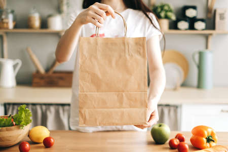 Caucasian woman hold eco shopping bag with fresh vegetables on the table in modern kitchen.の写真素材