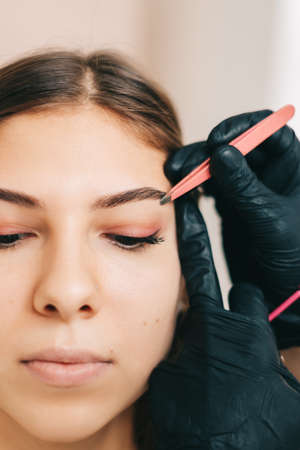 Eyebrow shaping procedure, make-up master uses tweezers and brush to shape the eyebrows. High quality photoの写真素材