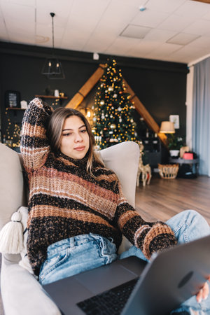 Young caucasian woman using laptop computer in holidays at home in the armchair in living room.の写真素材