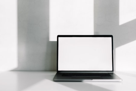 Laptop computer with white blank screen on the white table with shadow from window. High quality photoの写真素材