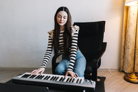 Young caucasian woman learns to play the piano keys using a laptop at home distantly. High quality...