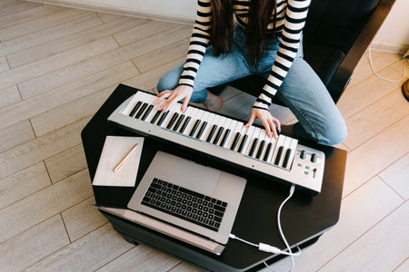 Young caucasian woman learns to play the piano keys using a laptop at home distantly. High quality photoの写真素材