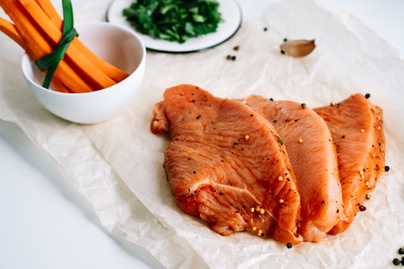 Marinated turkey steak with spices on a cooking paper with carrot sticks and herbs on the table. High quality photoの写真素材