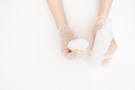 Womans manicurist hand in medical gloves. Holding a bottle with lotion or acetone, applying on cotton pad.の写真素材