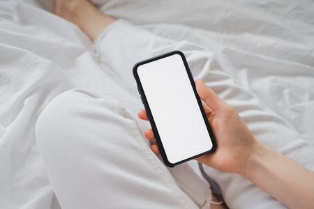Woman uses a smartphone with a white screen, sitting at home on a sofa in the morning. Mock up. High quality photo.の写真素材