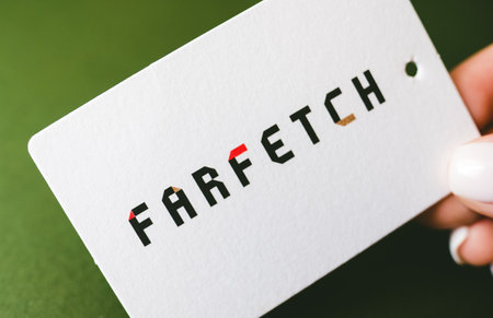 Hands holding Farfetch logo on green background, farfetch is online fashion store.