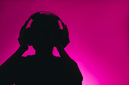 Dark silhouette of a female in headphones isolated on a pink background with copy space.の写真素材