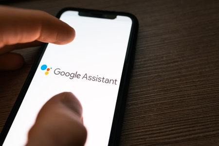 Smartphone with google assistant logo on the screen. hand touching the screen. High quality photo.のeditorial素材