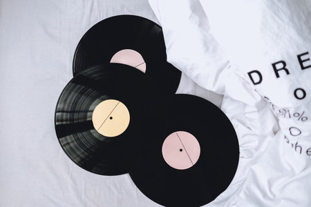 Old vinyl records stack on a white bed.